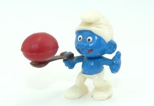 Diorama Eierlaufschlumpf mit Löffel und rotem Ei.  Figur ist schlierig bemalt und der Löffel ist verklebt.